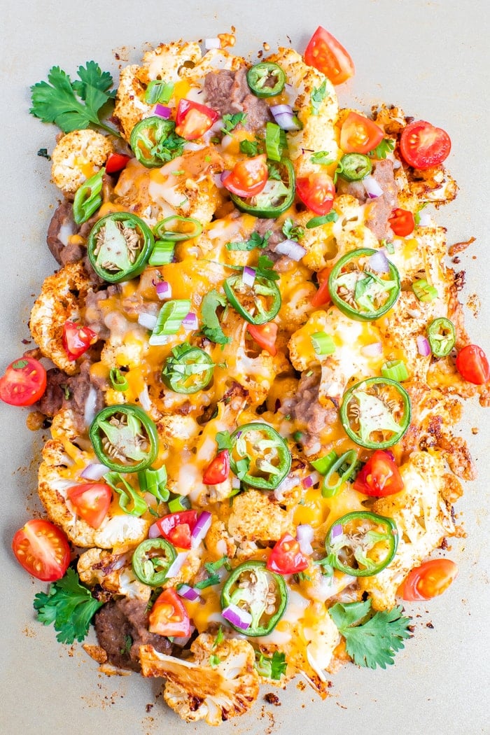 Cauliflower nachos baked on a sheet pan and topped with beans, cheese, onions, peppers and cilantro.
