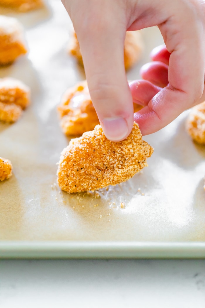 Hand placing an almond flour breaded chicken nugget on a baking sheet lined with parchment paper