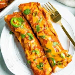 Two chicken enchiladas on a plate topped with cheese and cilantro with a fork on the plate.