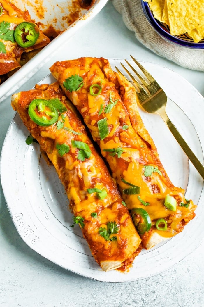 Two chicken enchiladas on a plate topped with cheese and cilantro.