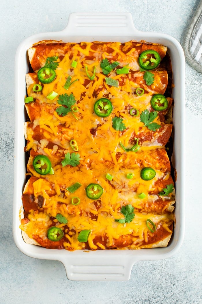 Baking casserole dish with cheesy chicken enchiladas topped with jalapeño.