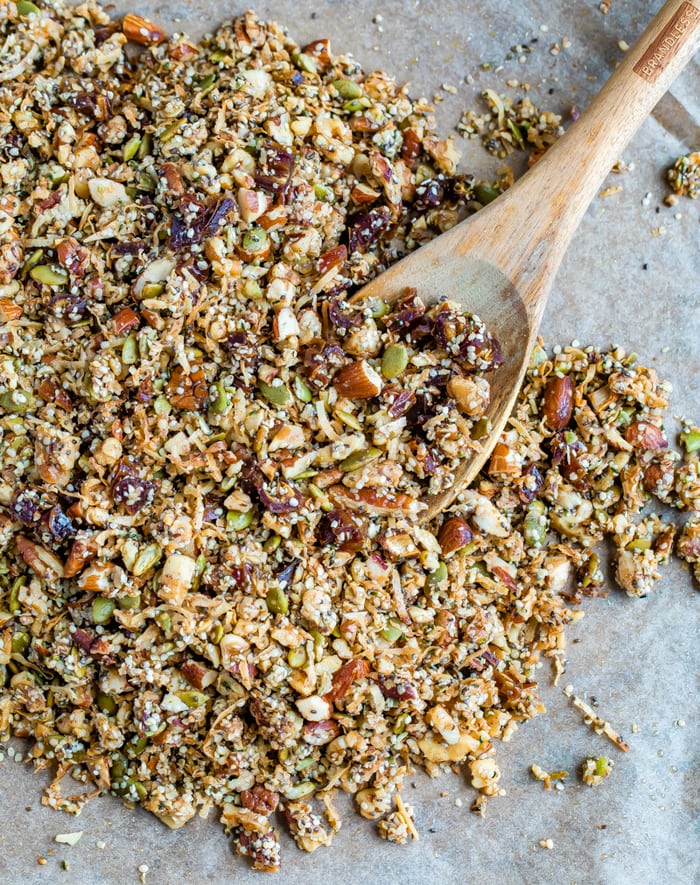 Hemp granola on a baking sheet lined with parchment paper. Wood spoon is on the sheet.