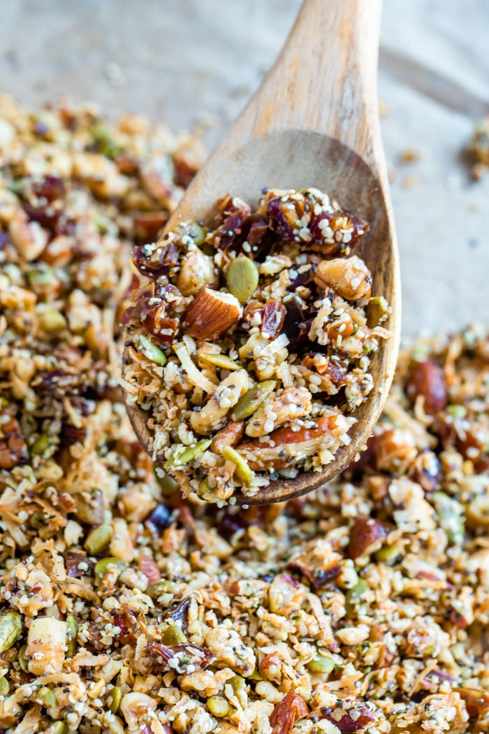 Wooden spoon scooping up hemp granola from a baking sheet lined with parchment paper.