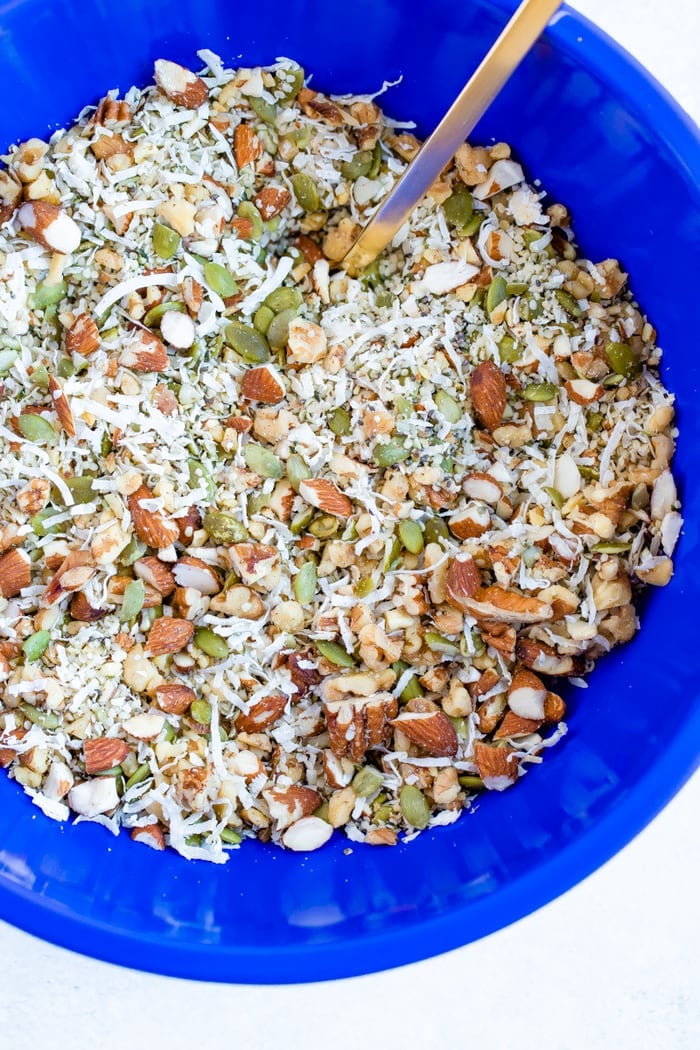 Blue mixing bowl wish ingredients for hemp granola including nuts, seeds and coconut flakes.