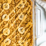 Glass dish with peanut butter banana baked oatmeal. Baked oatmeal is drizzled with peanut butter and slices of bananas.