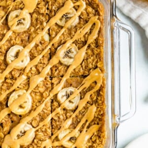 Glass dish with peanut butter banana baked oatmeal. Baked oatmeal is drizzled with peanut butter and slices of bananas.