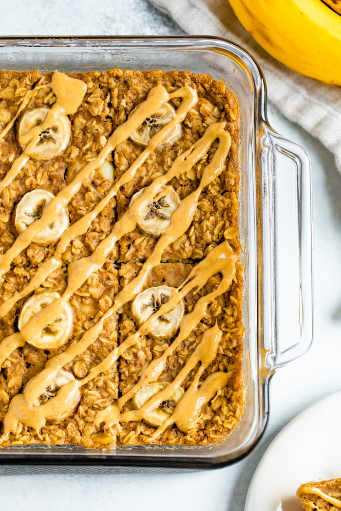 Glass dish with peanut butter banana baked oatmeal. Baked oatmeal is drizzled with peanut butter and slices of bananas.
