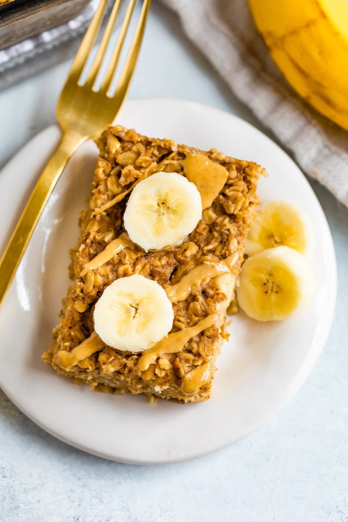 Slice of peanut butter banana baked oatmeal on a plate with a fork and topped with peanut butter drizzle and sliced bananas.