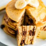 Stack of chocolate chip Greek yogurt pancaked topped with banana slices and with a bite of the stack taken out of it.