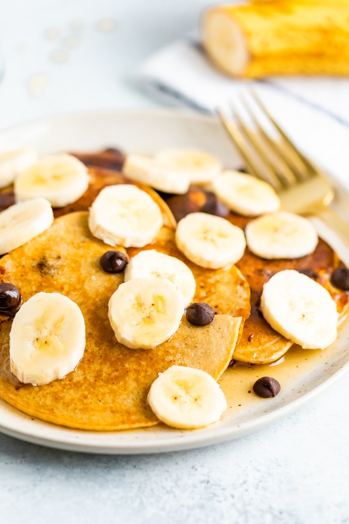 Greek yogurt pancakes on a plate topped with banana slices, chocolate chips and maple syrup.