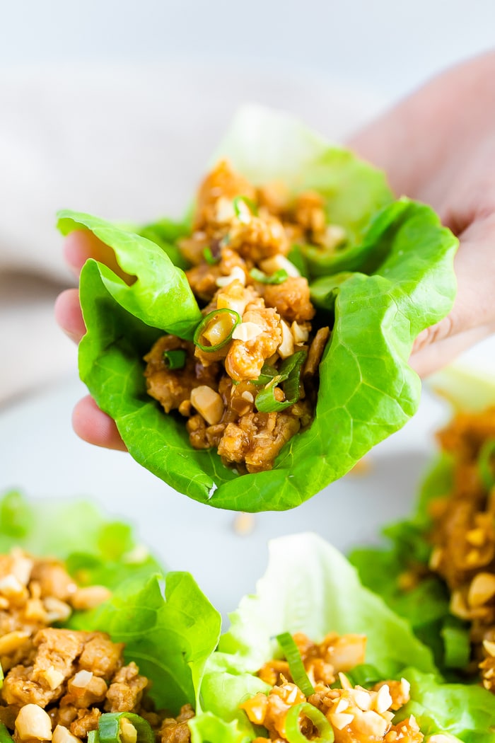 Hand holding a lettuce leaf filled with an Asian ground chicken filling.