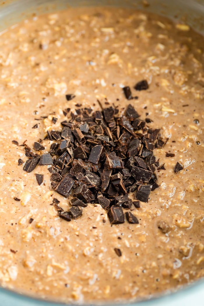 Mixture for chocolate baked oatmeal in a mixing bowl with chopped dark chocolate about to be mixed into the batter.