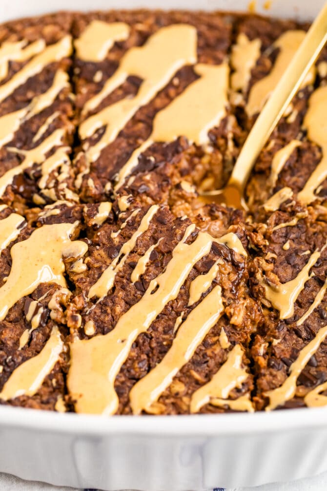 Baking dish with chocolate baked oatmeal cut into slices and drizzled with peanut butter.