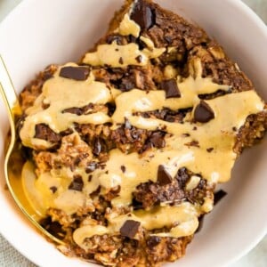 Slice of chocolate baked oatmeal in a bowl drizzled with peanut butter.