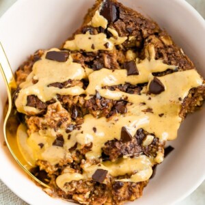 Slice of chocolate baked oatmeal in a bowl drizzled with peanut butter.