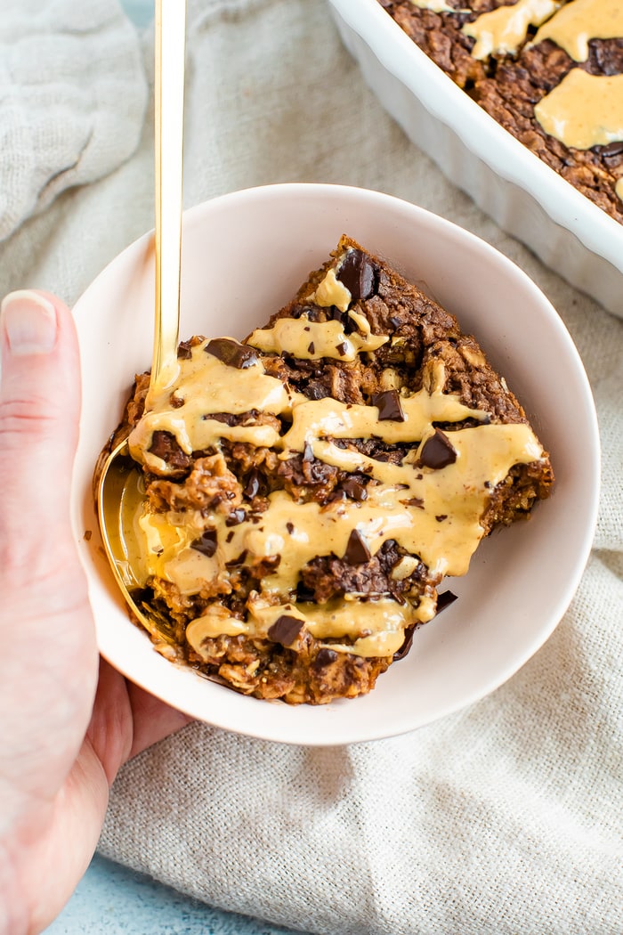Hand holding a bowl with a slice of chocolate baked oatmeal that is drizzled with peanut butter.