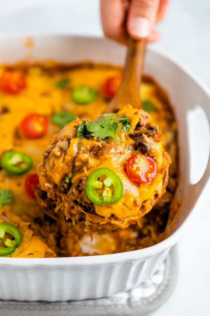 Wood spoon scooping a serving of cheesy spaghetti squash taco bake out of a casserole dish.