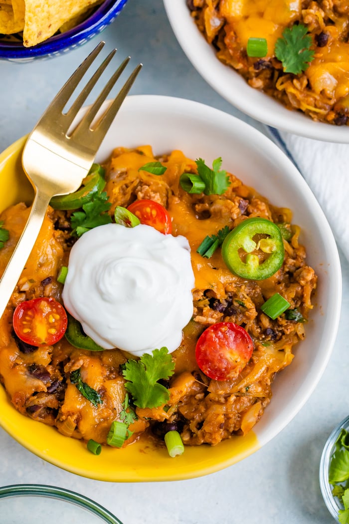 Bowl full of cheesy spaghetti squash taco bake topped with sour cream, tomatoes, jalapeños, green onions and cilantro.