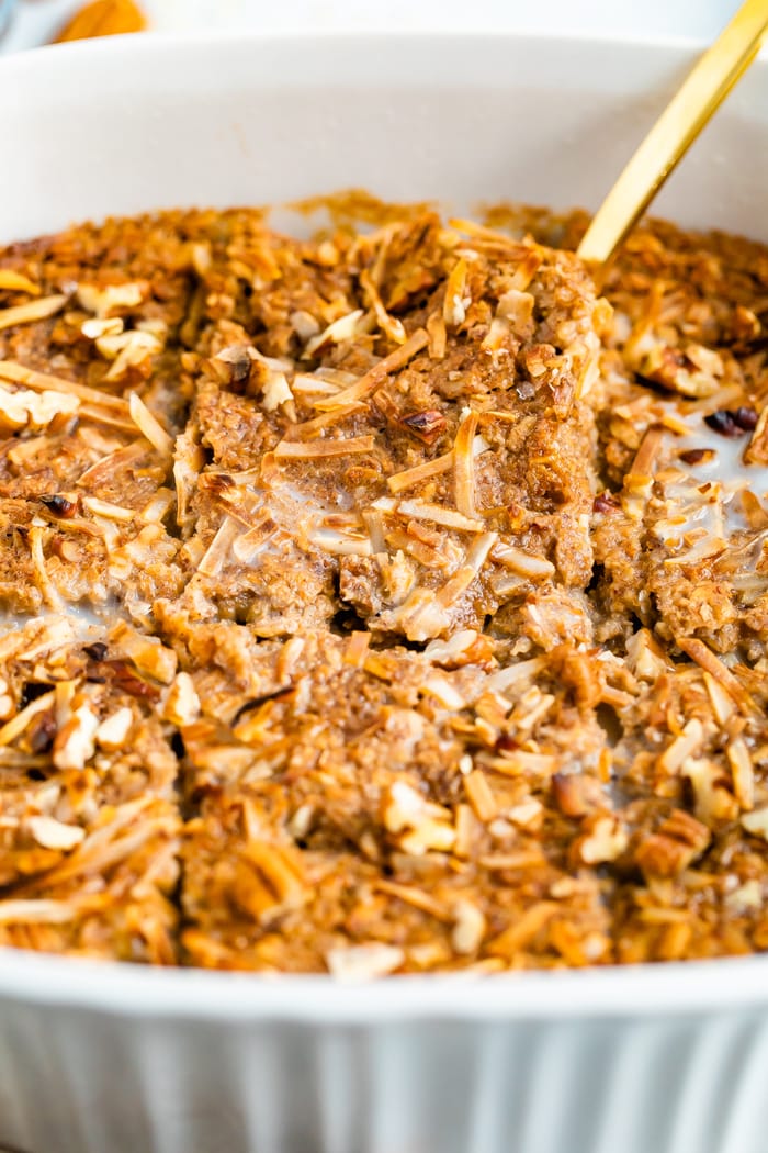 Baking dish with chai baked oatmeal sliced into 6 pieces. A serving spoon is in the dish.