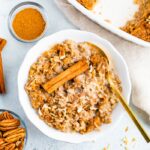 Bowl full of chai baked oatmeal topped with almond milk and a cinnamon stick.