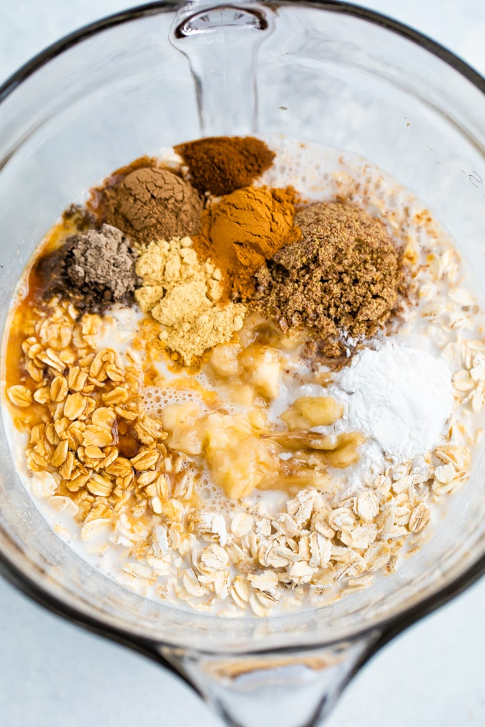 Glass mixing bowl with the ingredients and spices for chai baked oatmeal.