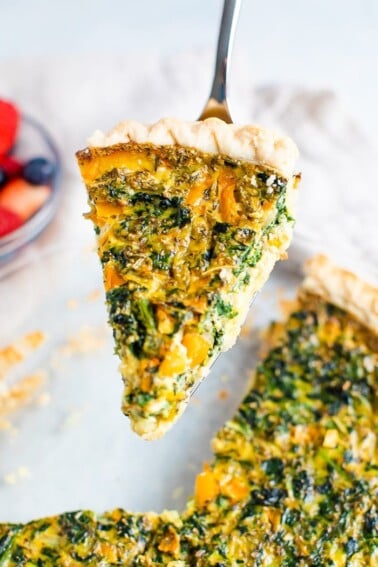 Spatula lifting a slice of spinach quiche from the pie.