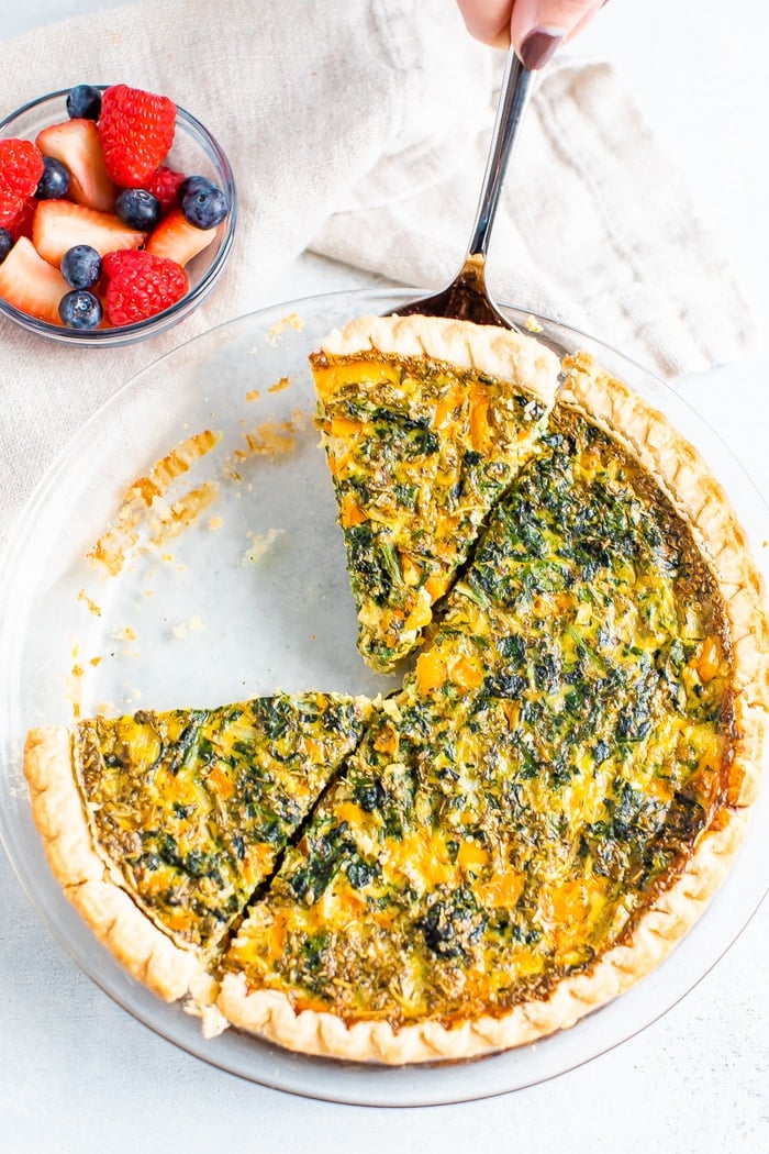 Spinach quiche with a spatula taking a slice out with a spatula. Bowl of berries is next to the quiche.