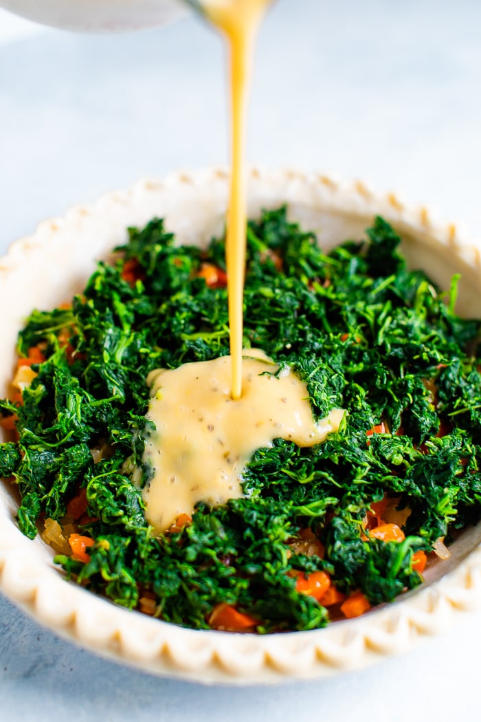 Egg mixture being poured over a quiche crust filled with spinach and bell peppers.