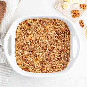 Baked oatmeal in a white baking dish with bananas and pecans.