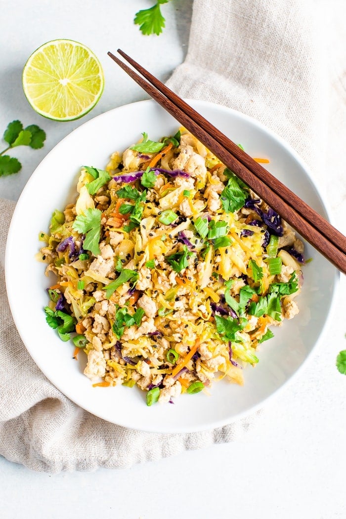 Ground poultry and coleslaw mix together in a bowl with chopsticks and topped with cilantro and lime.
