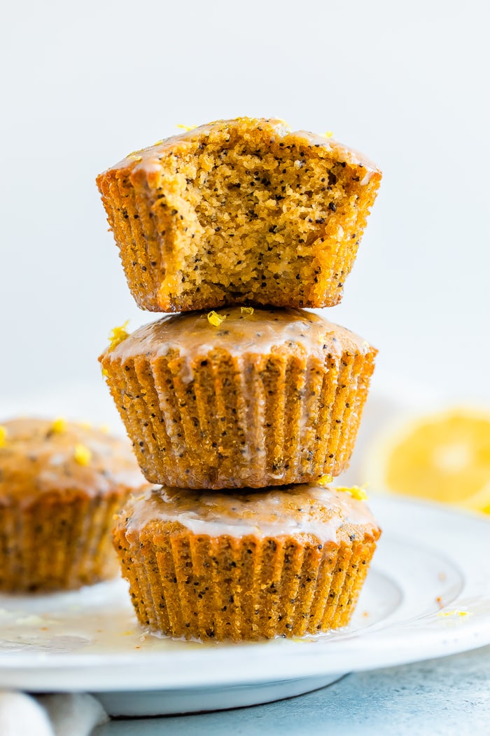 Stack of three lemon poppyseed muffins with a glaze. The top muffin has a bite taken out of it.