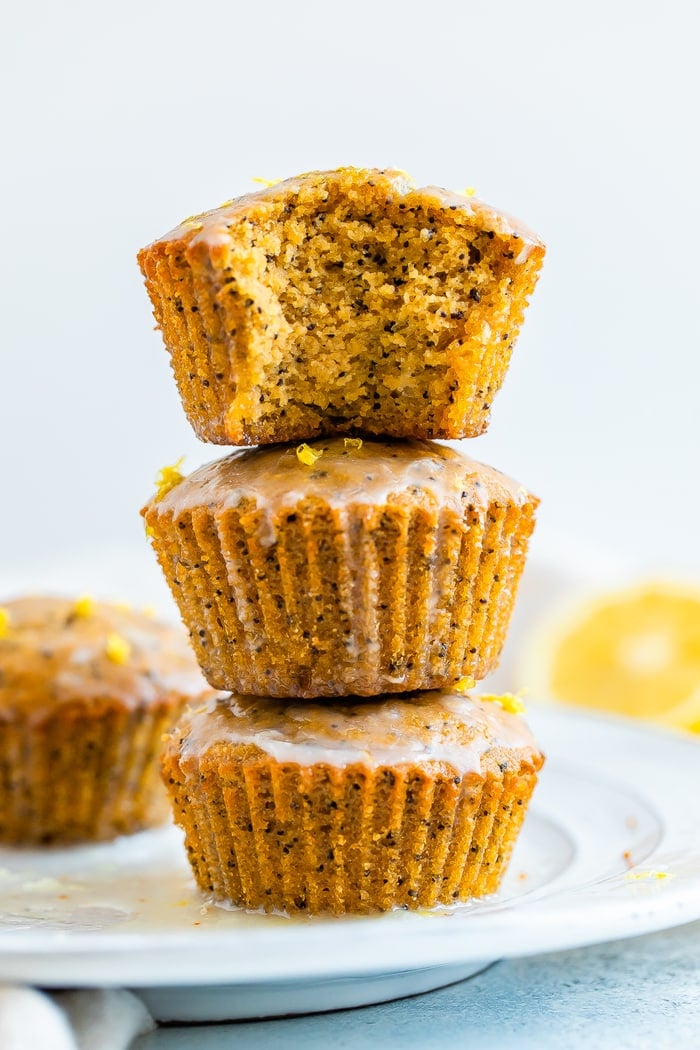 Stack of three lemon poppyseed muffins with a glaze. The top muffin has a bite taken out of it.