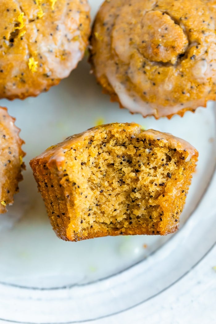 Lemon poppyseed muffins on a plate. One has a bite taken out of it.