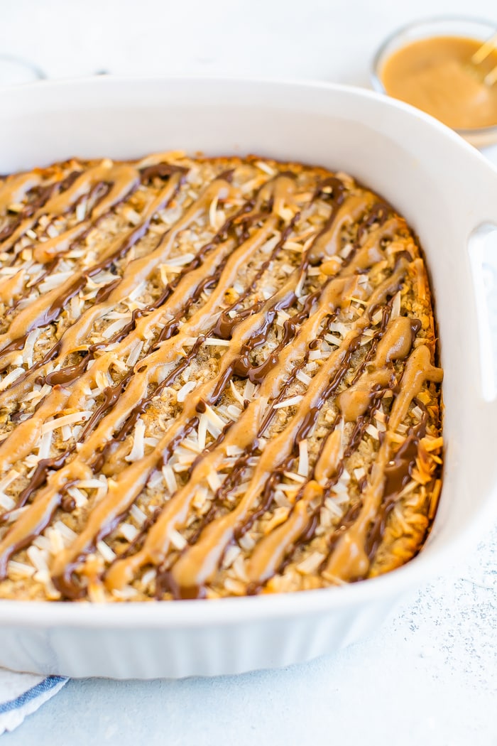 Baking dish with samoa baked oatmeal drizzled with date caramel and chocolate. Topped with toasted coconut flakes.