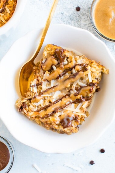 Slice of samoa baked oatmeal in a bowl with a gold spoon. Oatmeal is topped with coconut flakes and drizzles of caramel and chocolate.