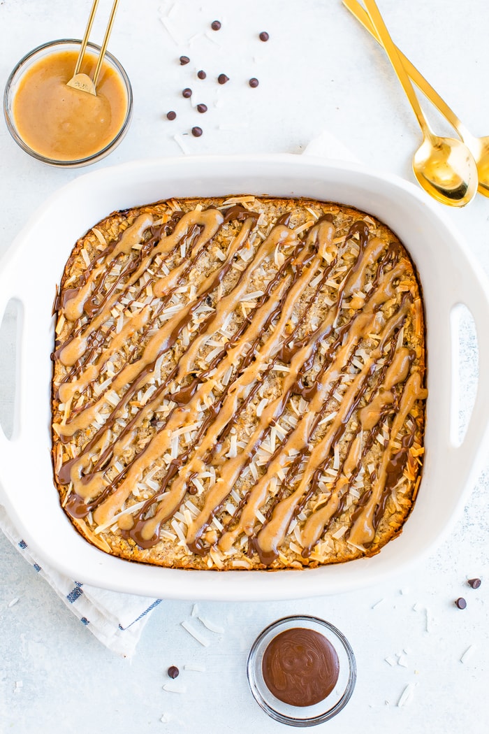 Square dish with baked oatmeal topped with caramel and chocolate drizzles and coconut flakes.