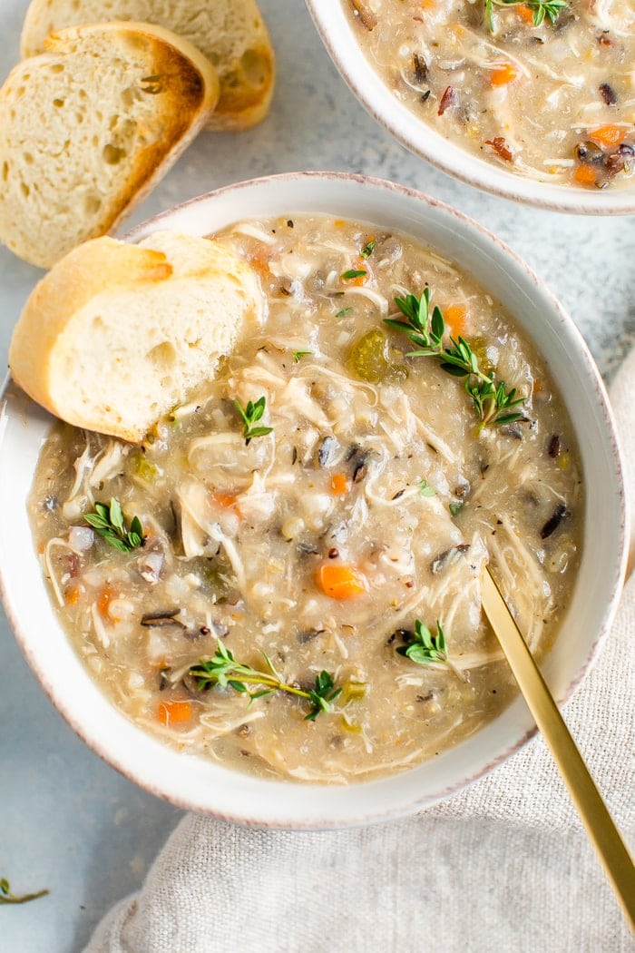 Bowl of wild rice chicken soup served with bread and fresh thyme.