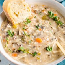Bowl of wild rice chicken soup served with bread and fresh thyme.
