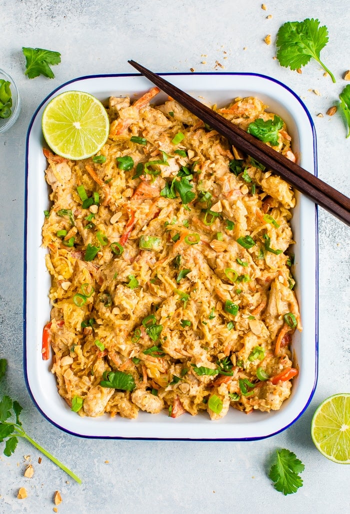 Rectangle serving tray full of spaghetti squash pad thai and topped with cilantro, peanuts, green onions and lime. Chop sticks are resting on the edge of the tray.