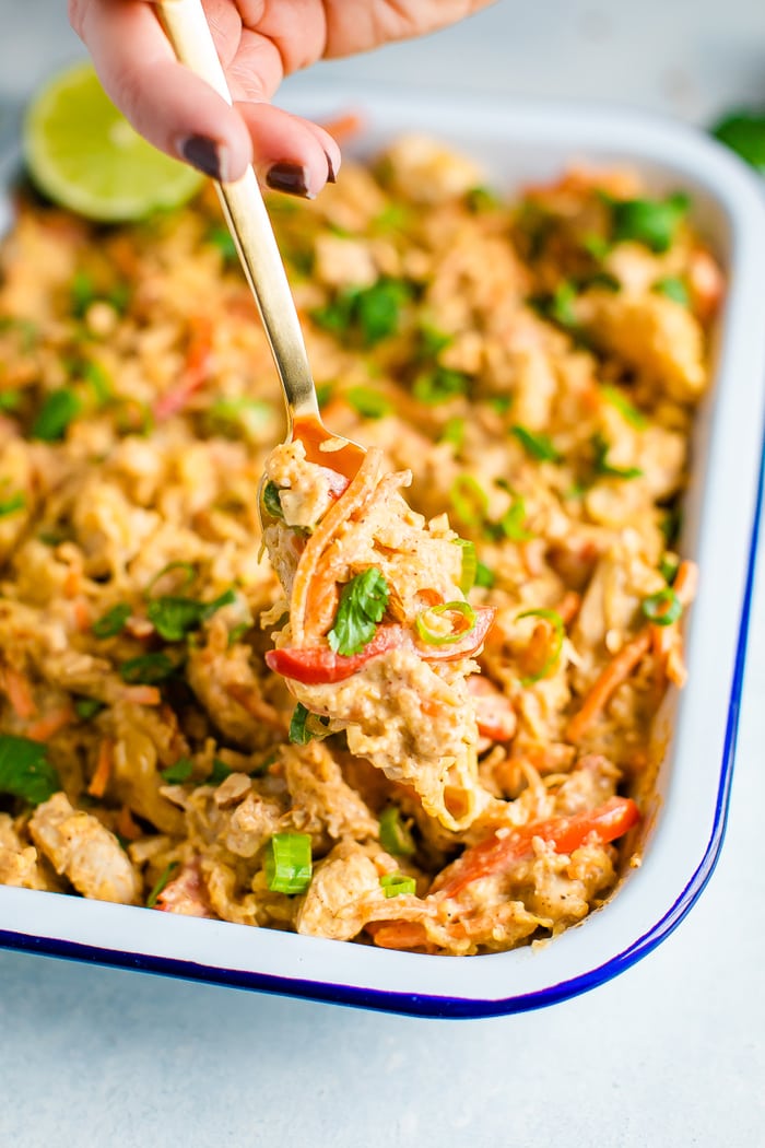 Hand scooping a bite on a fork of spaghetti squash chicken pad thai from a serving dish.