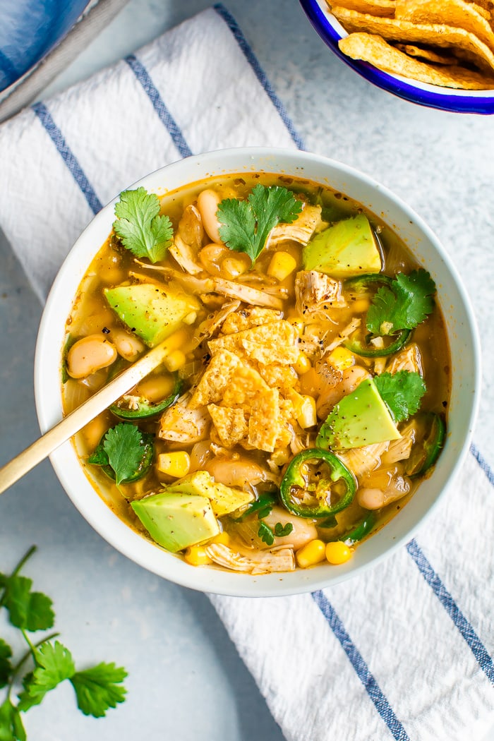 Bowl of white chicken chili topped with crumbled tortilla chips, avocado, jalapeño and cilantro.