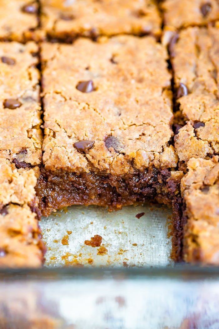 Gooey blondies in a pan cut into squares. One square is already taken.