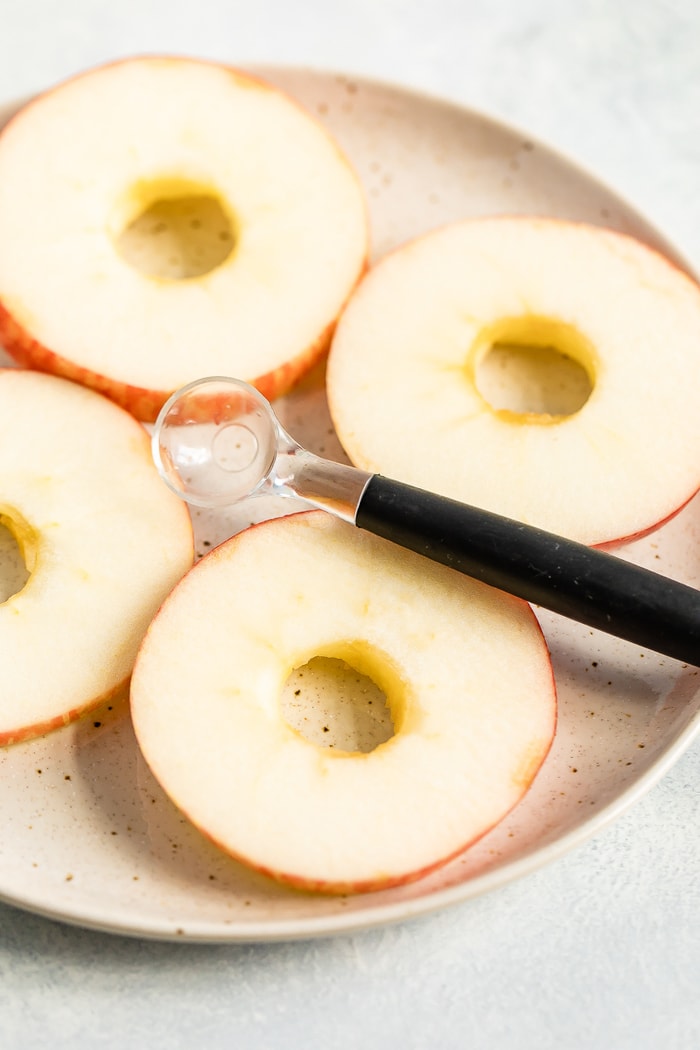 Four round slices of apples on a plate with the center core scooped out with a small melon baller so the apples look like rings.