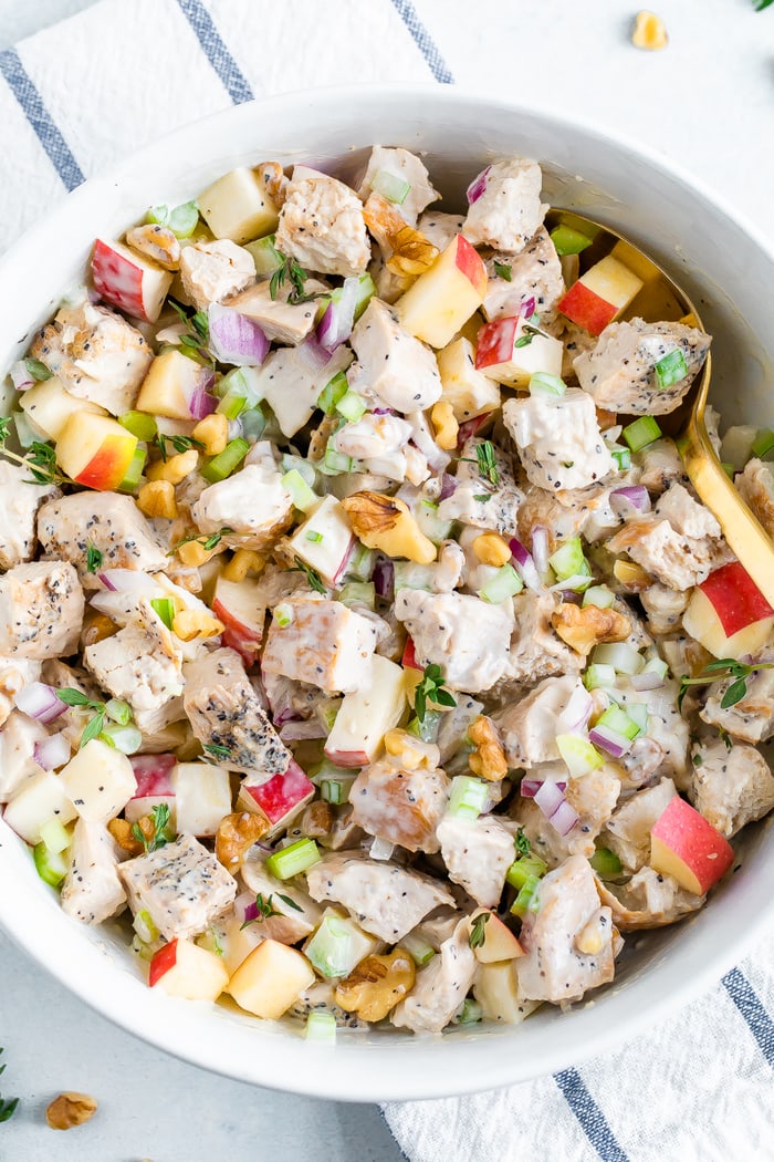 Bowl of chicken waldorf salad made with chunks of grilled chicken, chopped apple, celery, onion, herbs, walnuts and a creamy dressing.