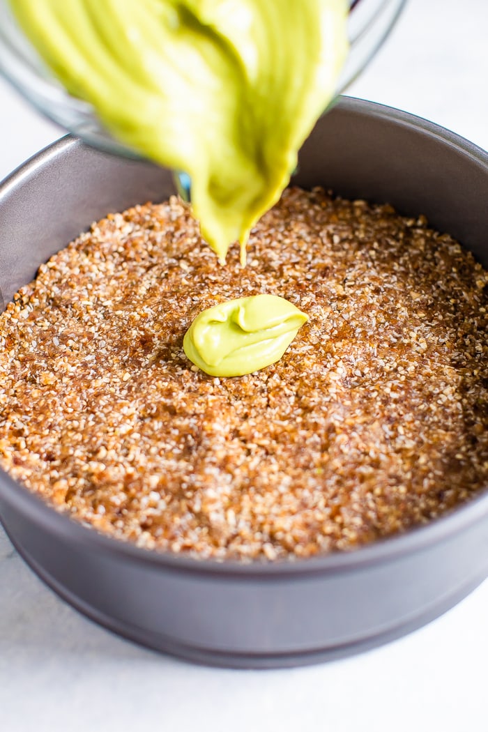 Blender pouring a creamy avocado lime filling into a spring form pan with a coconut pecan crust at the bottom