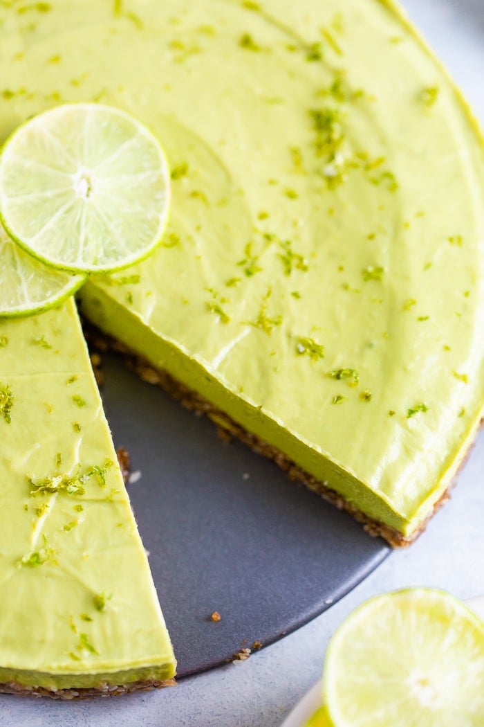 Avocado Lime tart topped with lime zest and lime slices with a slice cut out from it.