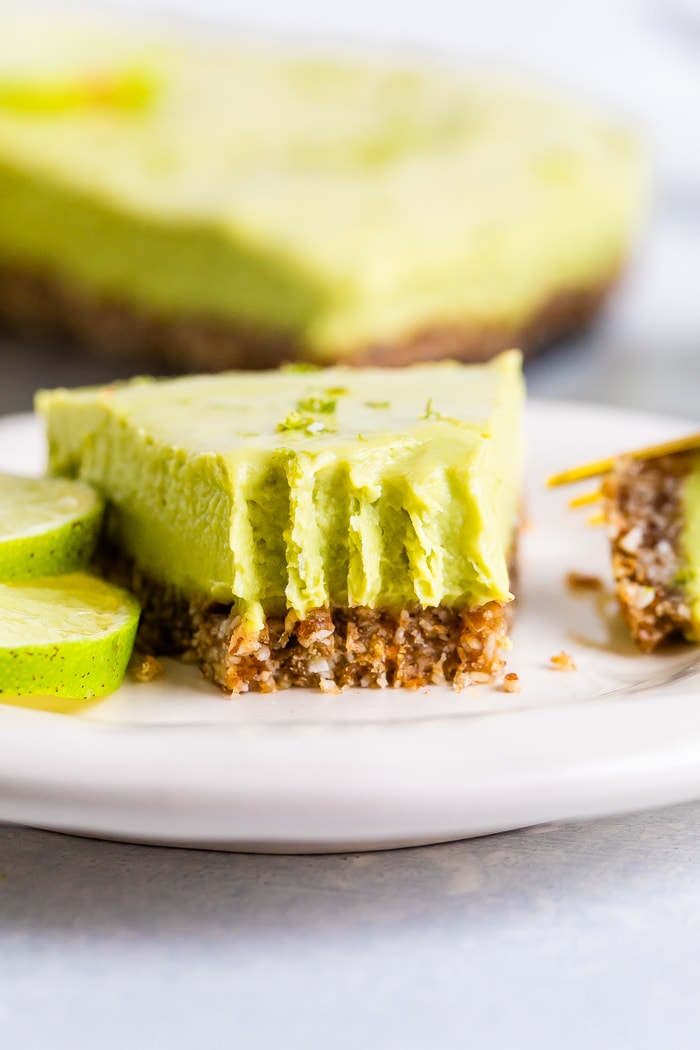 Slice of avocado lime tart on a plate with a fork bite taken out of it.