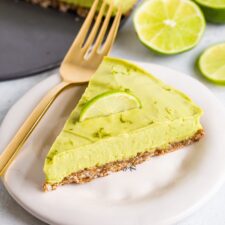 Slice of avocado lime tart on a plate with a fork and topped with lime zest and a lime slice.