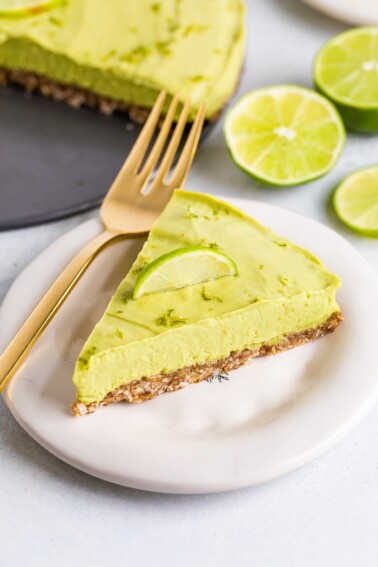 Slice of avocado lime tart on a plate with a fork and topped with lime zest and a lime slice.