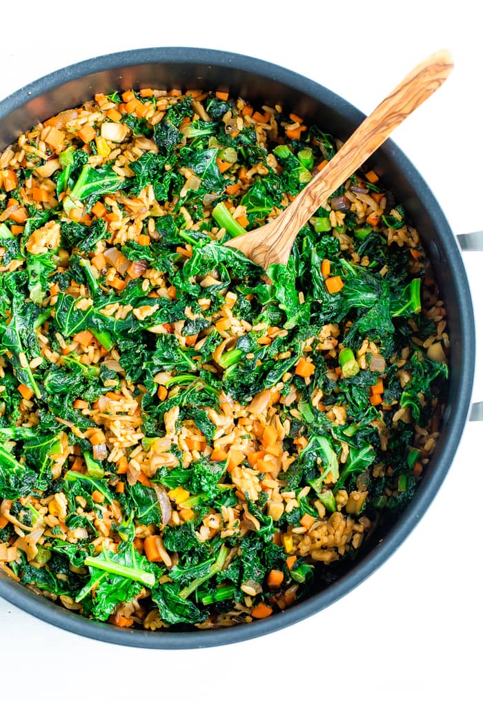 Skillet with a wood spoon stirring kale, veggies and rice.